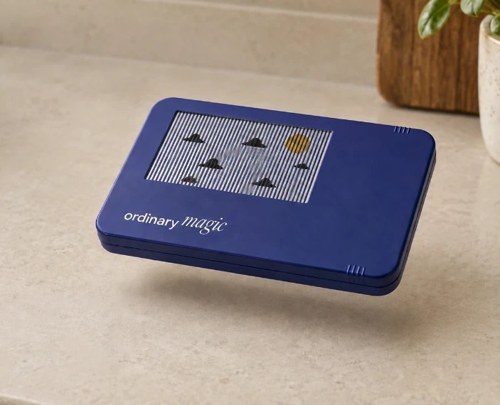 A navy Ordinary Magic tin with a striped picture window, floating just above a stone worktop.